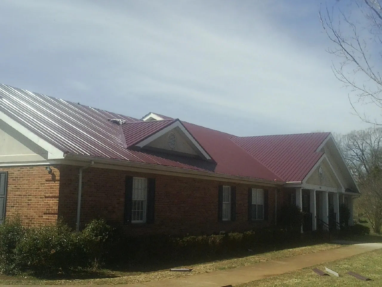 Red metal roof with gabled entries on a long brick building, from a Hail Damage Roof Repair job in Vance