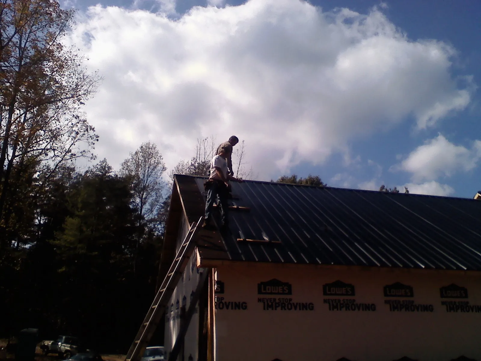 Roofer fastening dark metal panels high against a cloudy sky, from a Roof Inspection job in Vance