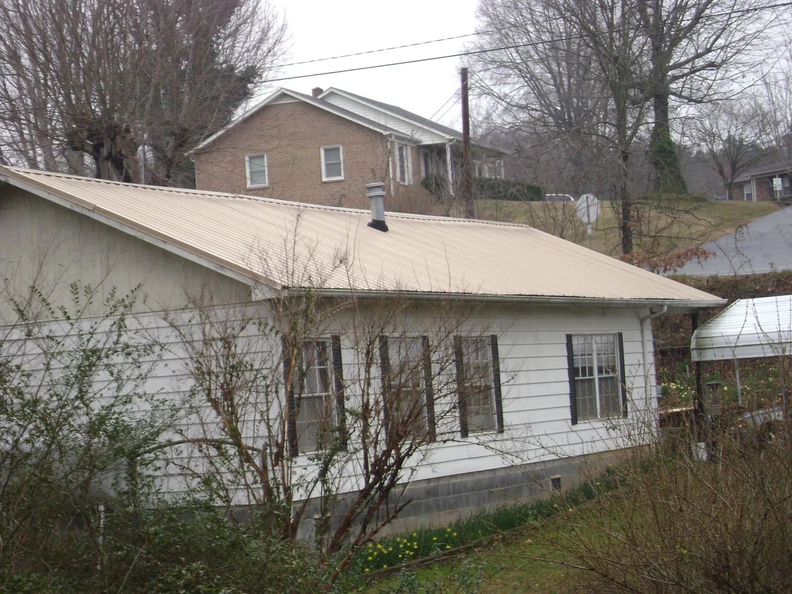 Tan metal roof on a white sided house set into a hillside — Commercial Roofing by Roofing Brothers in Vance