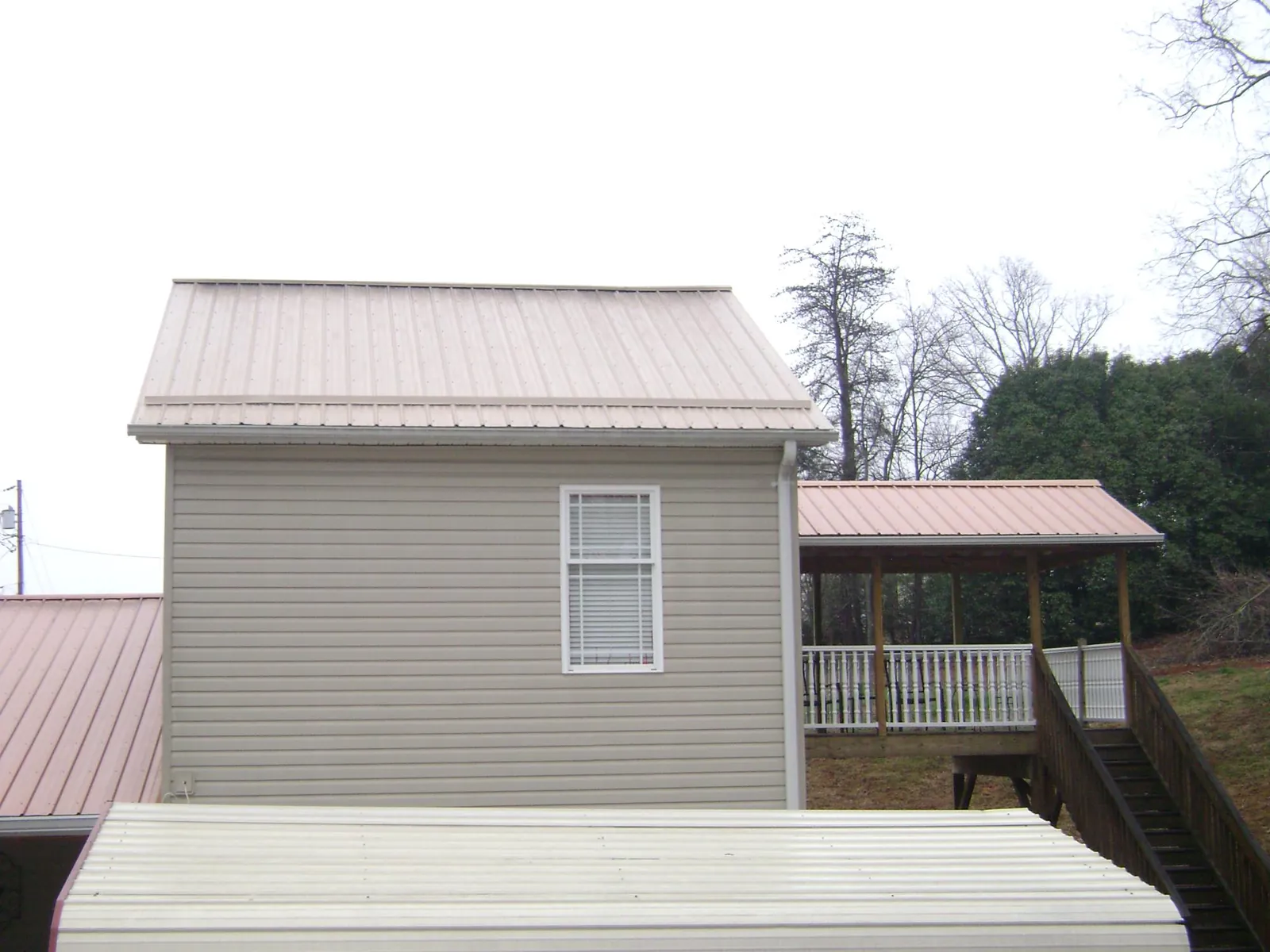 Tan metal roofs on a two story addition and attached porch, from a Roof Replacement job in Vance