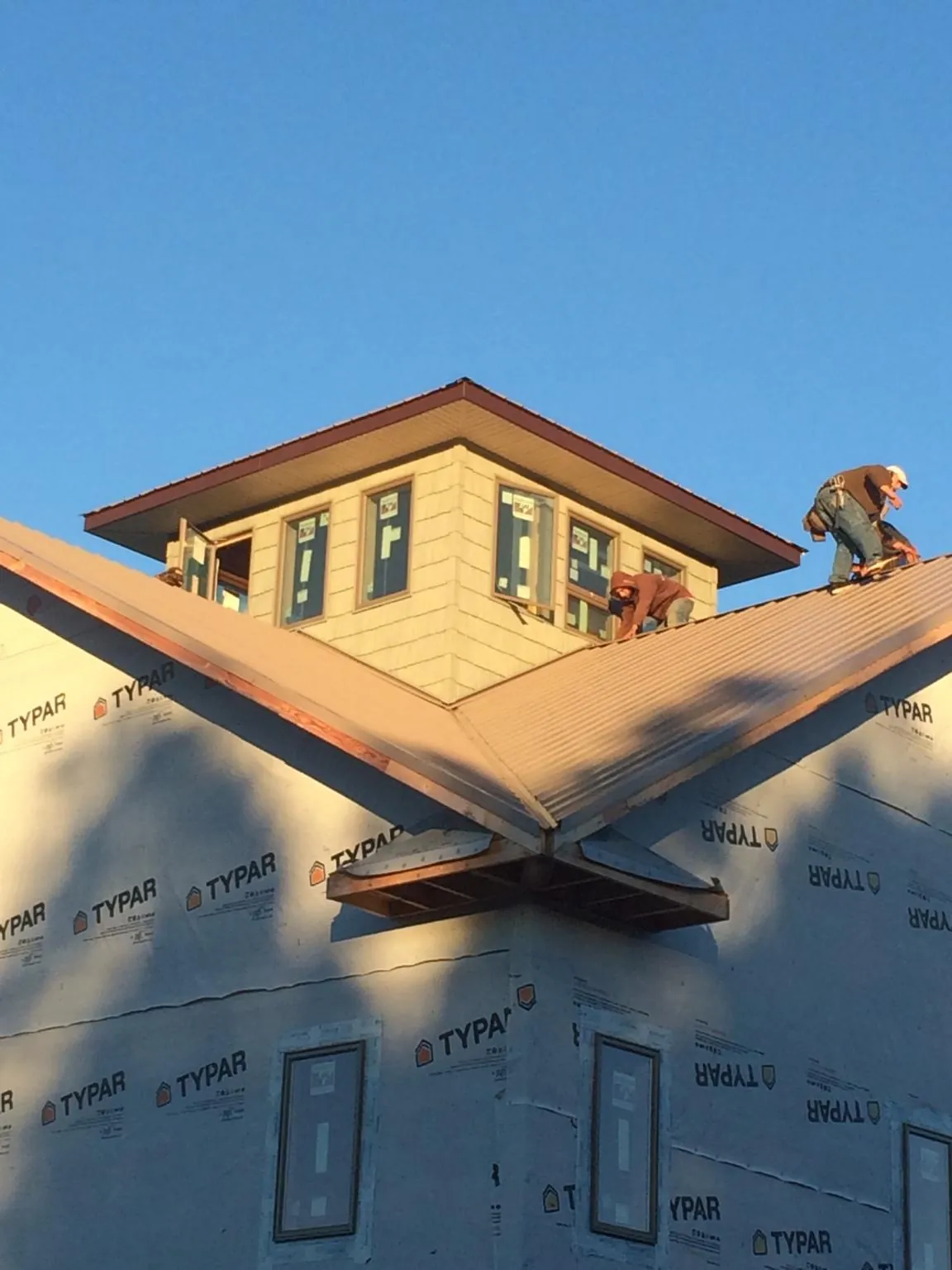 Roofers working around a rooftop cupola on a new metal roof at sunset — Roof Waterproofing in Vance by Roofing Brothers